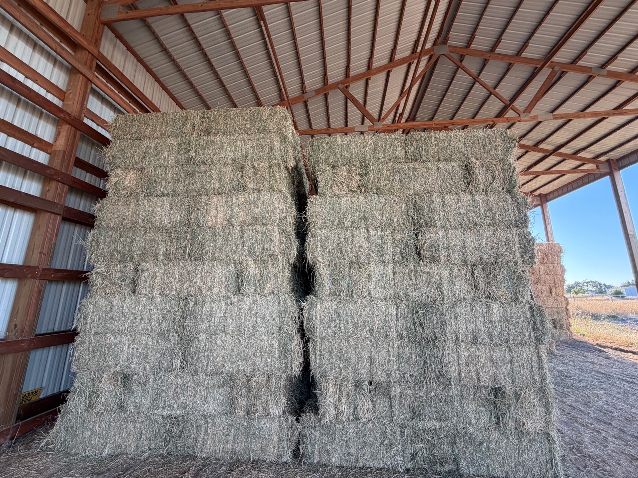 Small square alfalfa bales stacked inside a dry hay barn at Royer Ranch